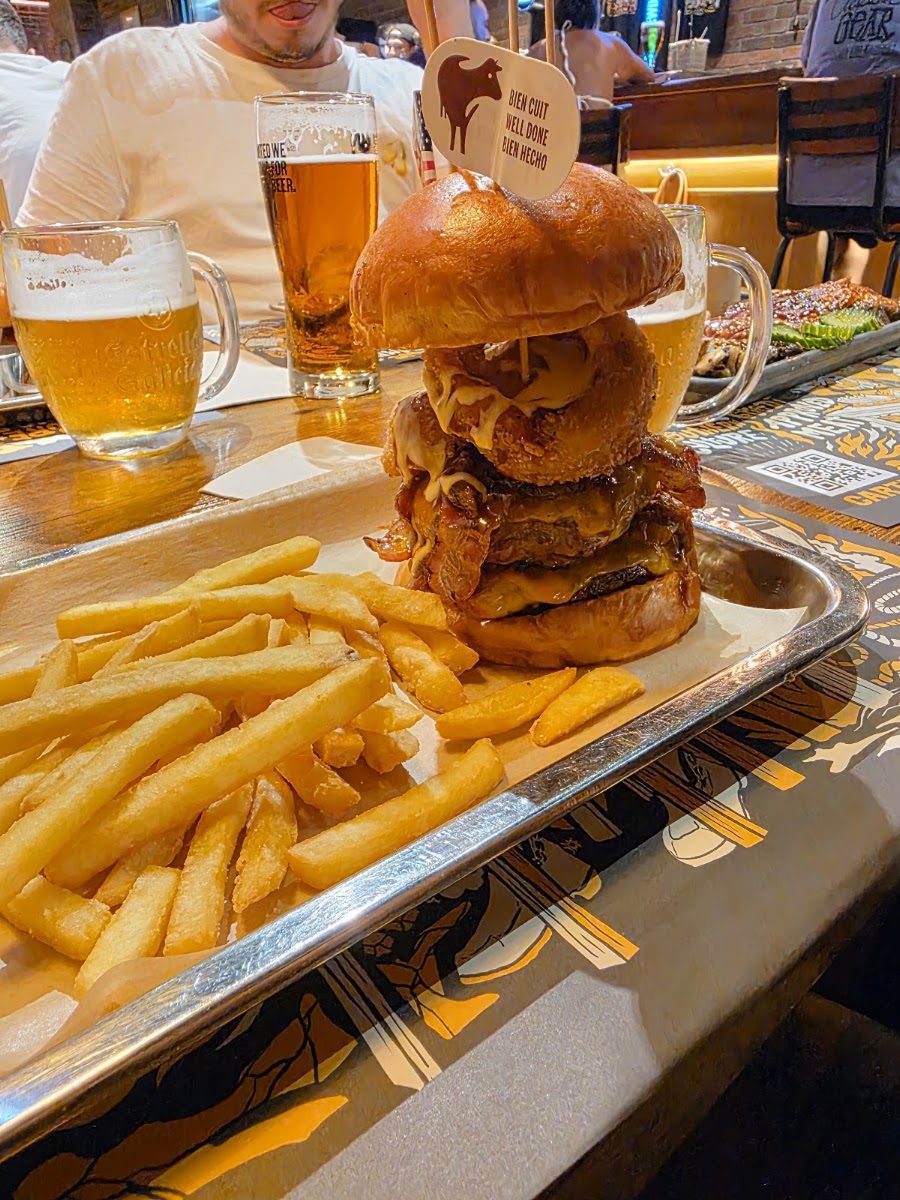 Burger alta con aros de cebolla junto a dos jarras de cerveza